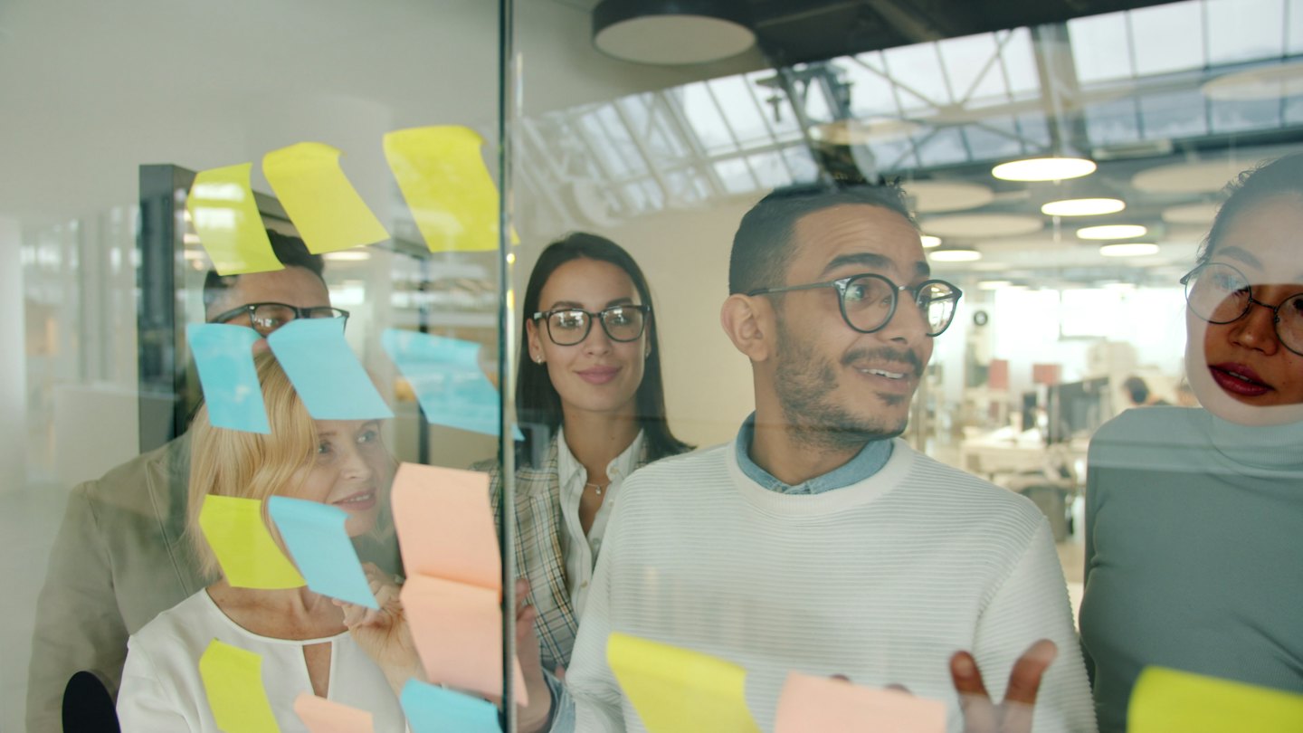 Équipe diversifiée réfléchissant à des idées avec des post-it sur du verre.